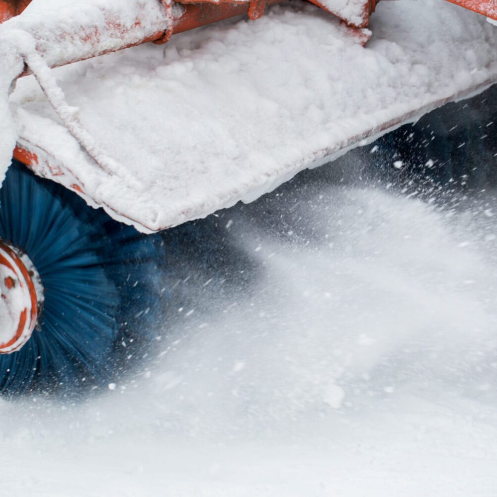 City service cleaning snow , a small tractor with a rotating brush clears a road in the city park from the fresh fallen snow on winter day