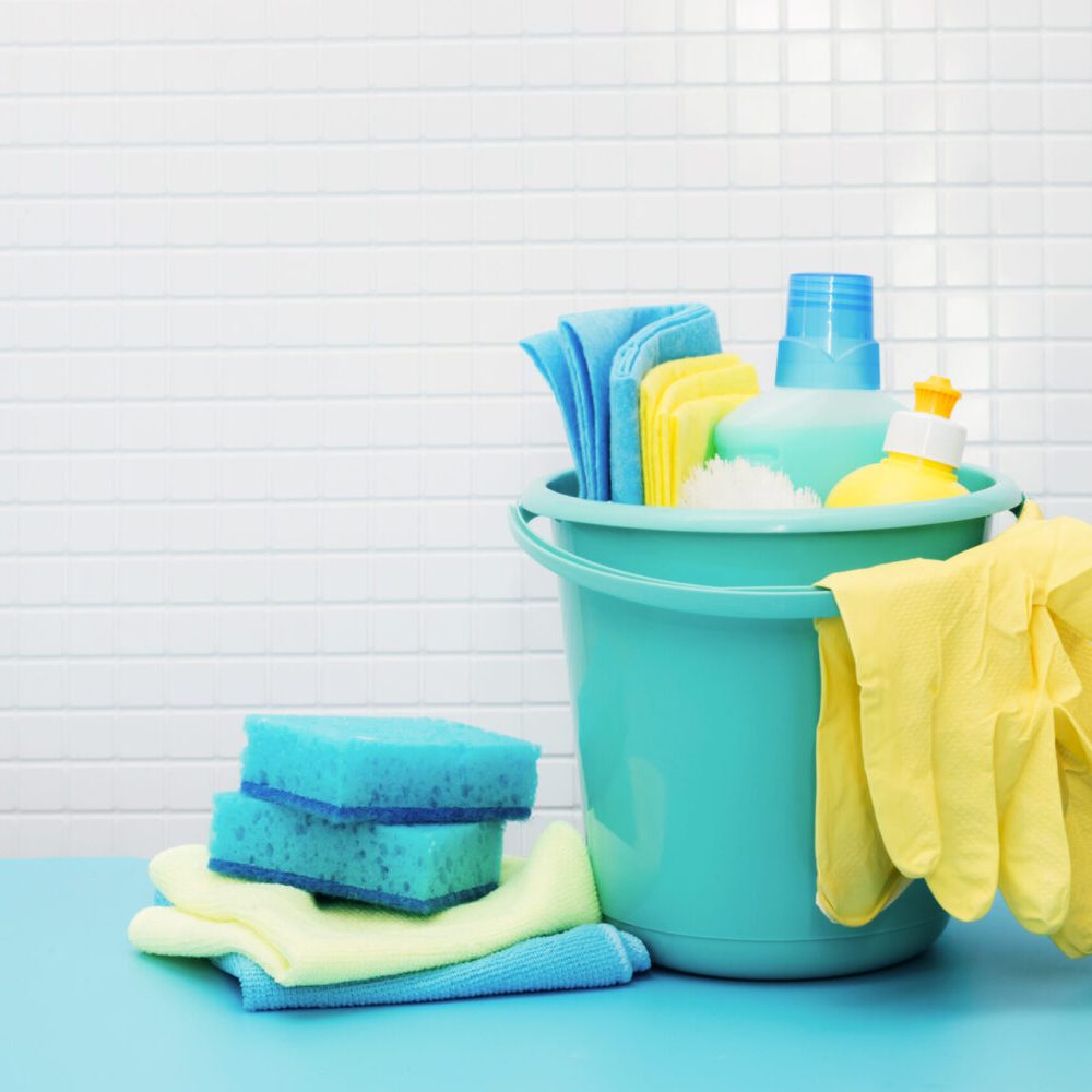 Cleaners and detergents in bucket, accessories for cleaning various surfaces and rooms blue background. The concept of cleaning in kitchen, bathroom, spring regular cleaning, cleaning company services