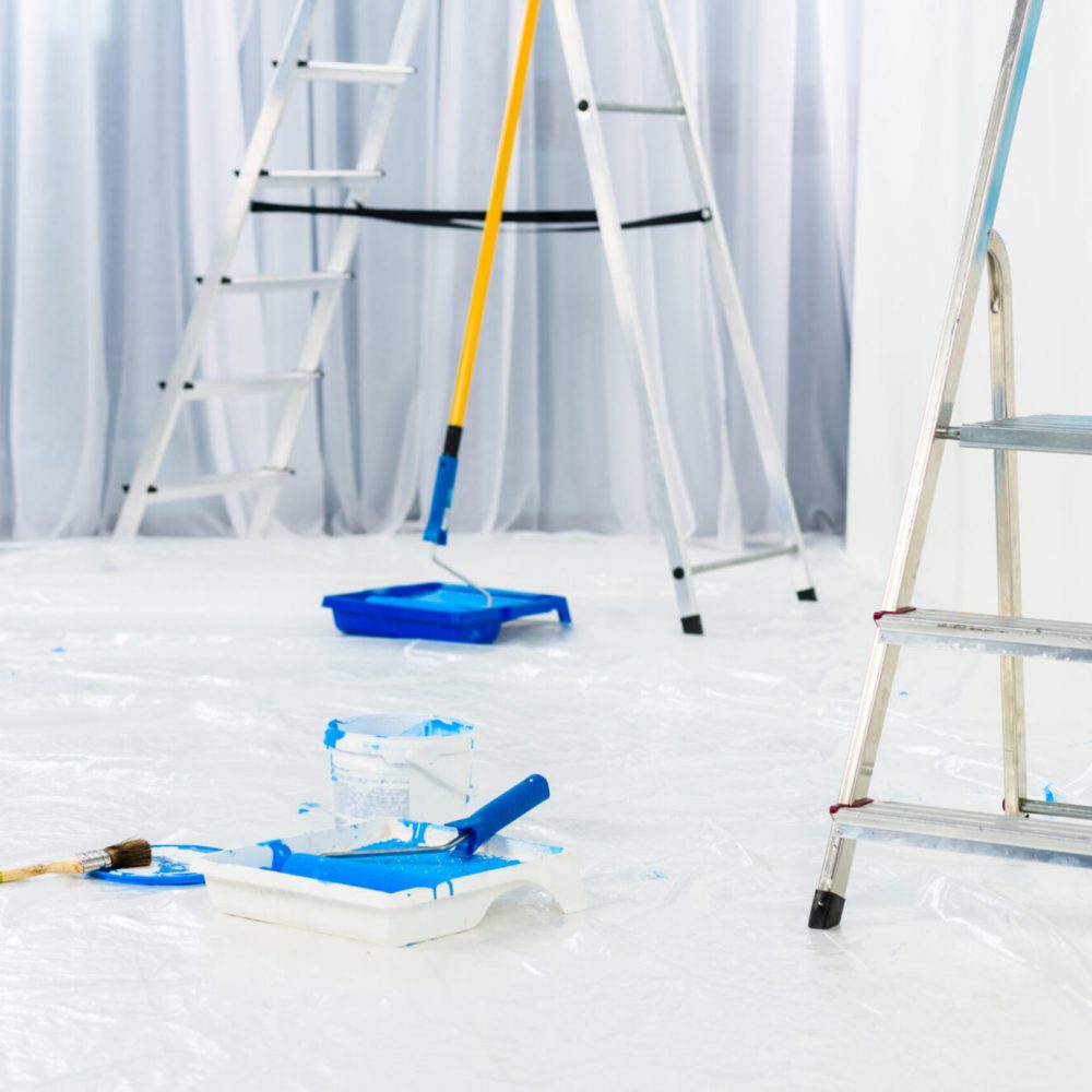 ladders and paint roller brushes in blue paint in room